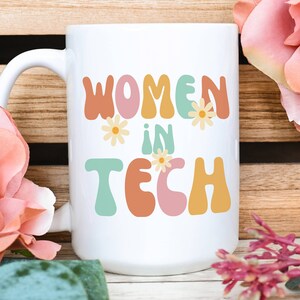 Puede incluir: Taza de cerámica blanca con el texto "Women in Tech" en letras coloridas de estilo retro y pequeños detalles de flores.
