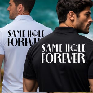 May include: Two golf polo shirts, one white and one black, with the phrase "SAME HOLE FOREVER" printed on the back in white. The design includes a golf ball graphic. The shirts have a collared neckline.