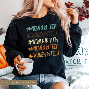 May include: Black sweatshirt with the text "#WOMEN IN TECH" repeated five times in different colors. The text is stacked vertically in a retro style font.