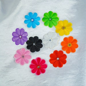 May include: Ten colourful embroidered flower shapes with a buttonhole in the centre. The flowers are in shades of pink, red, orange, yellow, green, blue, purple, white, and black.