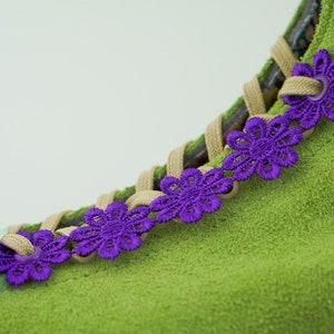 Könnte beinhalten: Grüner Wildlederschuh mit violetten Schnürsenkel-Akzenten. Die Schnürsenkel sind mit dekorativen violetten Blumen gebunden.