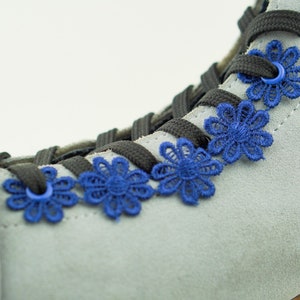 Könnte beinhalten: Grauer Wildlederskate-Stiefel mit schwarzen Schnürsenkeln und blauen Spitzenblumen-Akzenten.