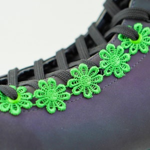 Könnte beinhalten: Ein Paar schwarze High-Top-Sneaker mit grünen Schnürsenkel-Akzenten. Die Schnürsenkel sind mit grünen, blumenförmigen Charms gebunden.