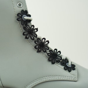 Pode incluir: Botas de couro cinza com detalhes de flores de renda preta nos cadarços.