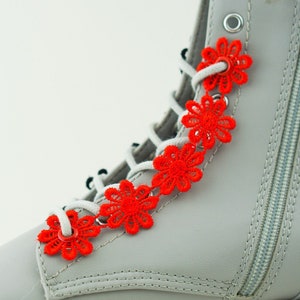 Könnte beinhalten: Graue Stiefeletten mit Reißverschluss an der Seite und roten Schnürsenkel-Akzenten in Form von Blumen.