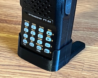 Pode incluir: Um transceptor FM Yaesu FT-60 preto com um visor digital que mostra "WW7PSA" e um teclado com botões etiquetados como "SQ TYP", "CODE", "TX PO", "MHz", "LOCK", "DTMF", "BAND DN", "BAND #", "P.SEL", "HMURV", "FWD". O transceptor está montado em um suporte de plástico preto.