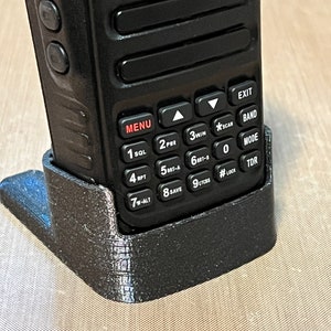 Pode incluir: Um r&aacute;dio bidirecional preto em um suporte preto. O r&aacute;dio possui um teclado com v&aacute;rios bot&otilde;es e uma tela. O suporte foi projetado para manter o r&aacute;dio em posi&ccedil;&atilde;o vertical. O r&aacute;dio tem a marca "Wouxun" impressa.