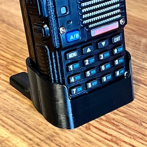 May include: A black handheld radio with a black charging stand. The radio has a keypad with buttons labeled 1-9, TDR, VOX, WN, ABR, TOT, BEEP, SAVE, SCAN, SOL, and EXIT. The radio also has a screen with the text "BAOFENG" and "VFO/MR".