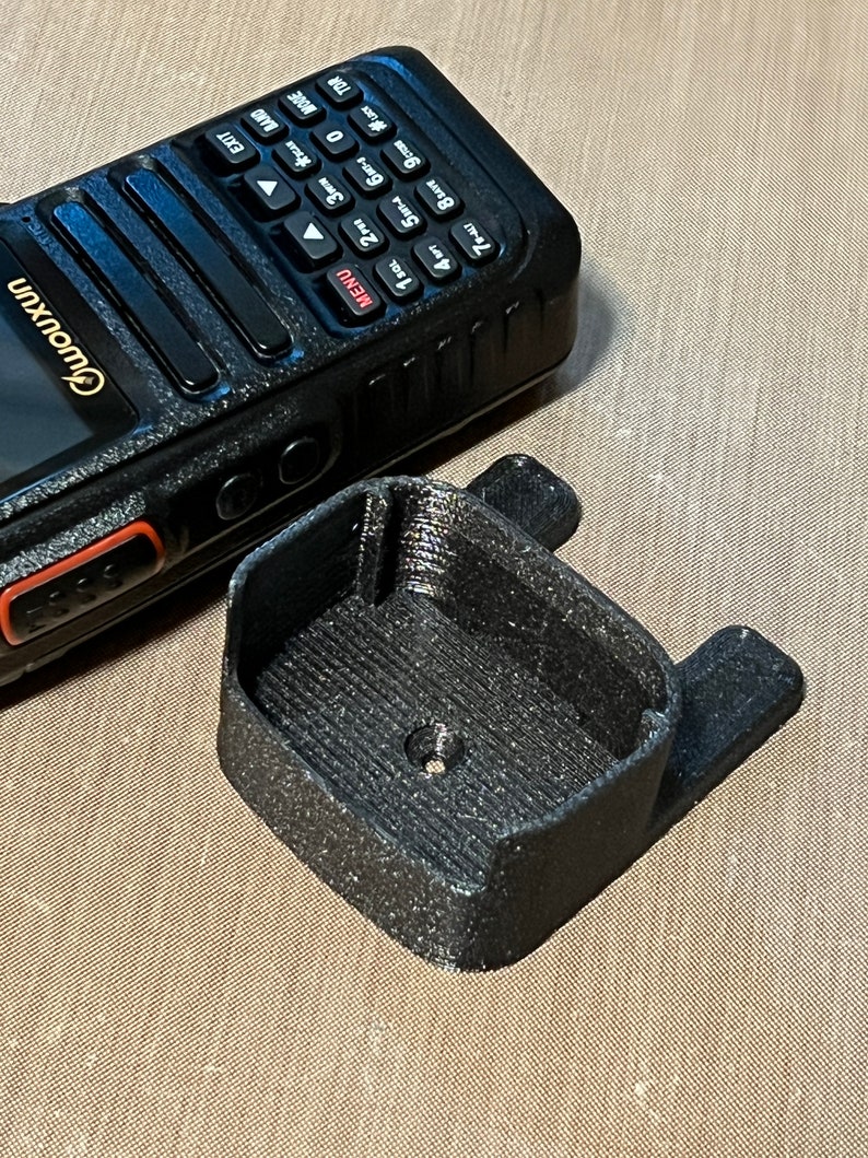 Pode incluir: Um r&aacute;dio port&aacute;til preto com teclado e tela, ao lado de um suporte preto impresso em 3D. O r&aacute;dio tem a marca "Owouxun". O suporte tem formato retangular com duas abas laterais. Dispositivo de comunica&ccedil;&atilde;o.
