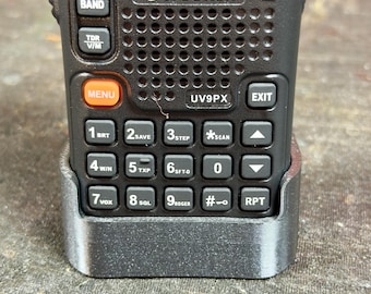 Pode incluir: Um rádio bidirecional preto Wouxun UV9PX com teclado e tela. O rádio tem botões rotulados como "BAND", "MENU" e "EXIT". O teclado inclui números e teclas de função. O rádio está em uma base de carregamento cinza.