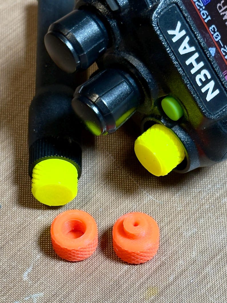 May include: A black handheld radio with the text "N3HAK" and black knobs. The radio has a yellow cap on the antenna and a yellow button. Two orange caps are also visible.