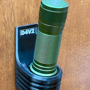 May include: A black 3D printed flashlight holder with the text "D4V2" on the side. A green flashlight is mounted in the holder.