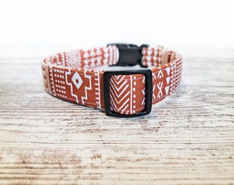 May include: A dog collar with a geometric pattern in shades of brown and white. The collar has a black plastic buckle and a matching black square loop. The fabric features repeating patterns of shapes and lines.