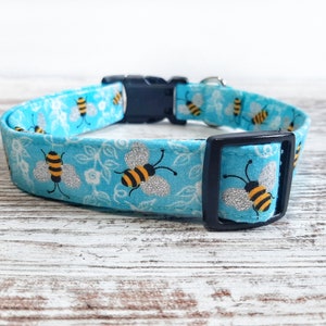 May include: A blue dog collar with a pattern of bees and silver glitter. The collar has a black buckle.