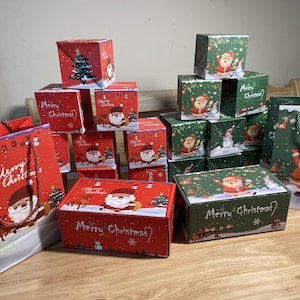 Może przedstawiać: Kolekcja świątecznych pudełek i torebek na prezenty. Pudełka są czerwone i zielone, z Mikołajem, choinkami i napisem "Merry Christmas". Torby na prezenty mają sznurkowe uchwyty i świąteczne wzory.