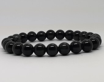 May include: A black beaded bracelet. The bracelet is made of polished, round, black beads strung together. The beads have a glossy finish and reflect light. The bracelet is displayed on a white surface.