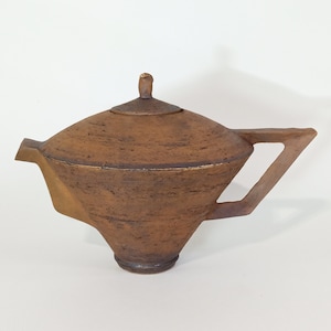 Pode incluir: Uma chaleira de cerâmica marrom com um design angular único. A chaleira tem uma tampa com uma pequena pega no topo e uma alça que se estende do lado.