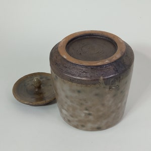 Op de afbeelding: Een bruine keramische pot met een deksel. De pot heeft een gespikkelde glazuur en een donkerbruine rand. Het deksel heeft een kleine knop bovenop.