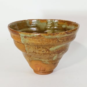 May include: A brown and green ceramic bowl with a wide rim and a flared base. The bowl has a rustic, hand-thrown look.