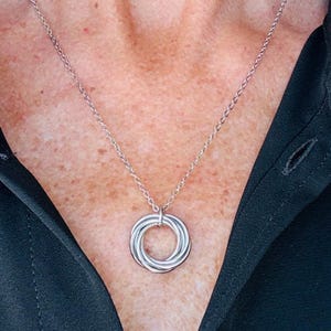May include: A silver-toned necklace featuring a pendant composed of three interlocking circular rings. The pendant hangs from a delicate, thin silver-toned chain. The design consists of smooth, polished metal loops that are connected together.