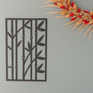 Peut inclure: Panneau décoratif mural en forme de bambou gris foncé avec un motif découpé. Le panneau rectangulaire présente des tiges et des feuilles de bambou stylisées. Une couronne de fleurs séchées aux accents rouges et dorés est suspendue en haut à droite.