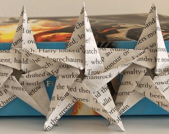 Puede incluir: Tres estrellas de papel blanco hechas con páginas de libros, con el texto "HARRY POTTER" visible en la portada azul del libro detrás de ellas.