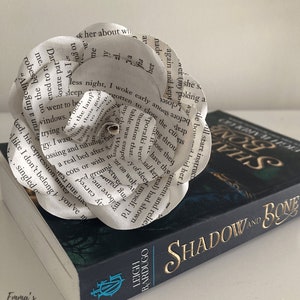Puede incluir: Una flor de papel blanca hecha con las p&aacute;ginas de un libro titulado "Shadow and Bone" de Leigh Bardugo. La flor est&aacute; encima del libro.