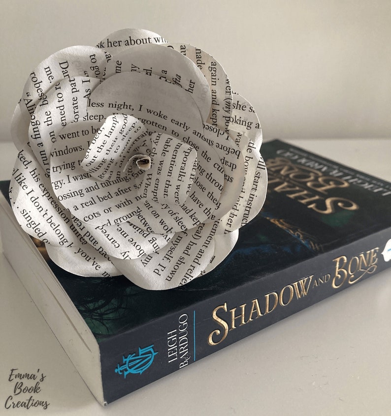 Puede incluir: Una flor de papel blanca hecha con las p&aacute;ginas de un libro titulado "Shadow and Bone" de Leigh Bardugo. La flor est&aacute; encima del libro.