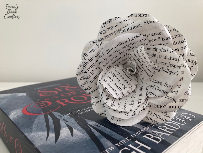 Puede incluir: Una flor de papel blanco hecha con las p&aacute;ginas de un libro. La flor est&aacute; encima de un libro titulado "Six of Crows" de Leigh Bardugo.