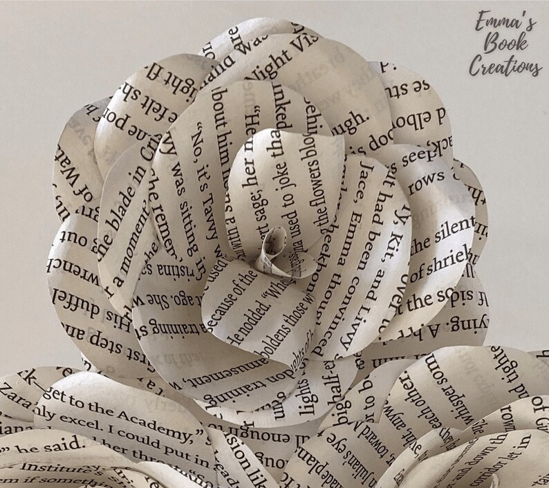 Puede incluir: Una rosa blanca de papel hecha con las p&aacute;ginas de un libro. La rosa est&aacute; compuesta por muchas capas de papel, cada una con texto impreso. La rosa es una obra de arte hermosa y &uacute;nica.