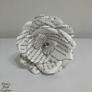 Puede incluir: Una flor de papel blanca hecha con las p&aacute;ginas de un libro. La flor est&aacute; compuesta por varias capas de papel, cada una con texto impreso. La flor est&aacute; enfocada, y el fondo est&aacute; desenfocado.