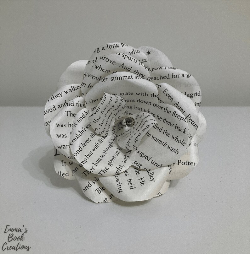 Puede incluir: Una flor de papel blanca hecha con las p&aacute;ginas de un libro. La flor est&aacute; compuesta por varias capas de papel, cada una con texto impreso. La flor est&aacute; enfocada, y el fondo est&aacute; desenfocado.
