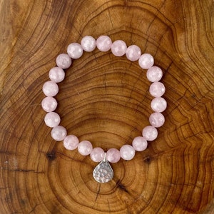May include: A pink rose quartz bracelet with a silver charm. The bracelet is made of faceted beads and is strung on elastic.
