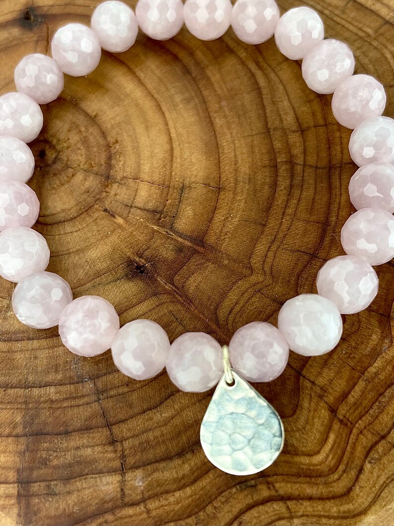 May include: A pink gemstone bracelet with a hammered silver teardrop charm. The bracelet is made of faceted beads and is strung on elastic.