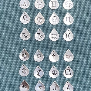 May include: A set of 20 silver teardrop-shaped charms with various symbols engraved on them, including zodiac signs, religious symbols, and other designs.