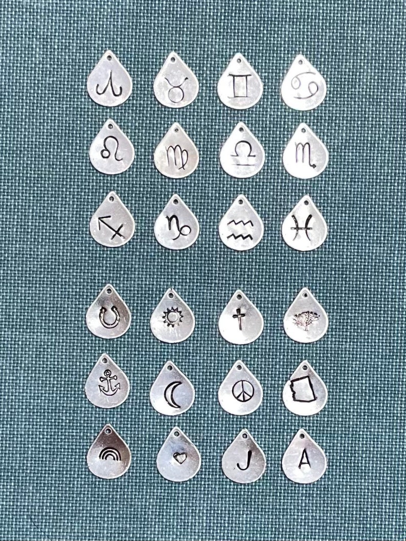 May include: A set of 20 silver teardrop-shaped charms with various symbols engraved on them, including zodiac signs, religious symbols, and other designs.