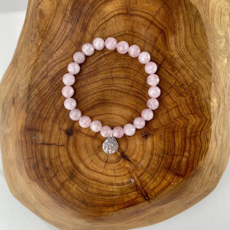 May include: A pink rose quartz bracelet with a silver charm. The bracelet is made of faceted beads and is strung on elastic.