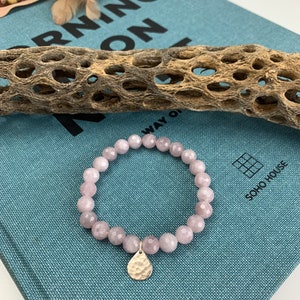 May include: A pink gemstone bracelet with a hammered silver charm. The bracelet is on a blue fabric surface with the text "Morning On" visible.
