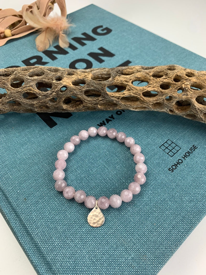 May include: A pink gemstone bracelet with a hammered silver charm. The bracelet is on a blue fabric surface with the text "Morning On" visible.