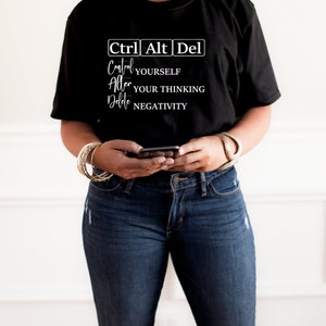 May include: A black t-shirt with the text "Ctrl Alt Del" and the words "Control Yourself", "Alter Your Thinking", and "Delete Negativity" written below. The shirt is being worn by a person with a brown hat.