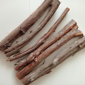 Puede incluir: Cinco ramas de madera marrón y desgastadas, dispuestas en forma de cruz sobre una superficie blanca.