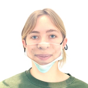 May include: A person wearing a face mask with a printed image of a face. The mask is light blue and has a black elastic band. The person is wearing a green shirt.