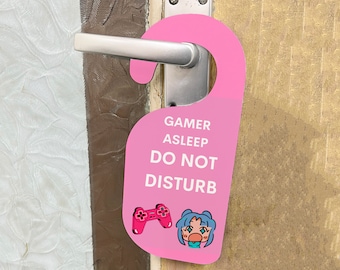 Könnte beinhalten: Rosaer Türhänger mit dem Text "Gamer Asleep Do Not Disturb" und einem Cartoon-Bild eines Spielers mit einem Videospiel-Controller.