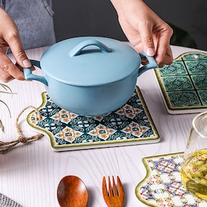 Puede incluir: Tres salvamanteles de cer&aacute;mica con intrincados dise&ntilde;os inspirados en azulejos en tonos de verde, azul, naranja y blanco. Los salvamanteles tienen forma de rect&aacute;ngulos irregulares con esquinas redondeadas. Una olla de cer&aacute;mica azul con tapa se encuentra sobre uno de los salvamanteles.