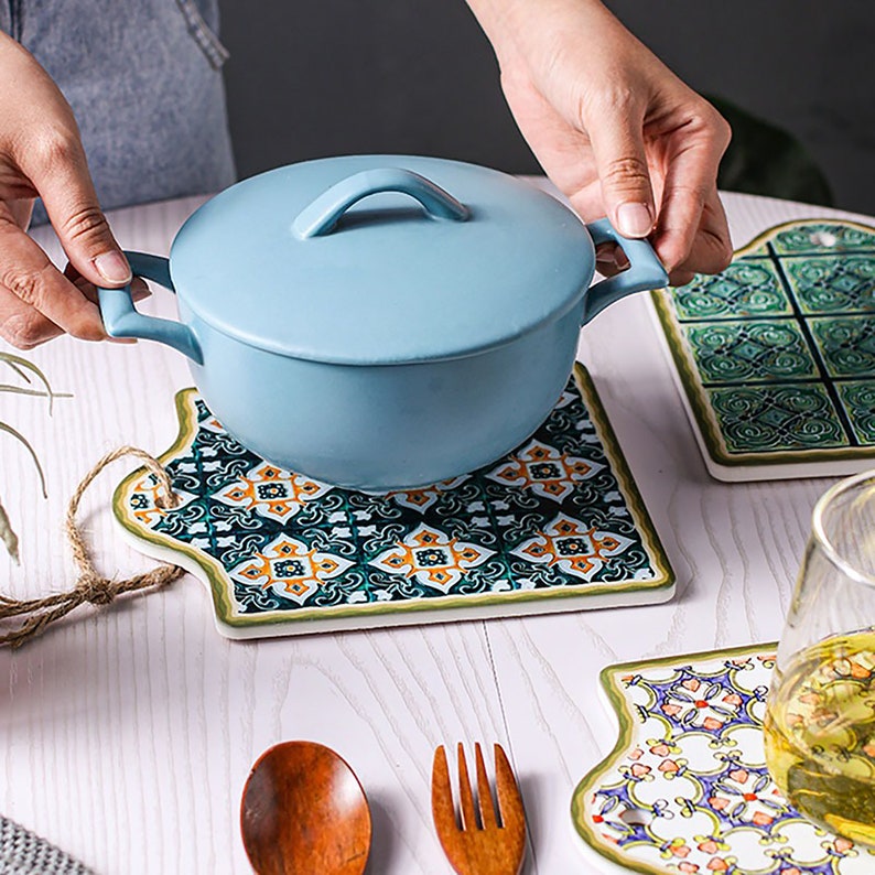 Puede incluir: Tres salvamanteles de cer&aacute;mica con intrincados dise&ntilde;os inspirados en azulejos en tonos de verde, azul, naranja y blanco. Los salvamanteles tienen forma de rect&aacute;ngulos irregulares con esquinas redondeadas. Una olla de cer&aacute;mica azul con tapa se encuentra sobre uno de los salvamanteles.