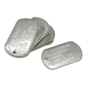 May include: A stack of silver dog tags with the text "SIMON RILEY GHOST 19119151618 TASK FORCE 141 BLOOD TYPE 0-" on one tag and "J. SILVERHARD ROCKERBOY SAMURAI BLOOD: A NEG REBEL SPIRIT" on another tag.