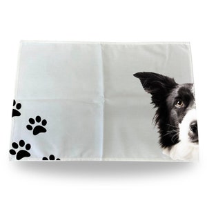 May include: White kitchen towel with black paw prints and a black and white border collie dog peeking from the right side.