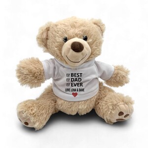 Könnte beinhalten: Ein beiger Teddybär, der ein weißes T-Shirt mit dem Text "BEST DAD EVER" und "LOVE LENA & DAVE" mit einem roten Herzen trägt.