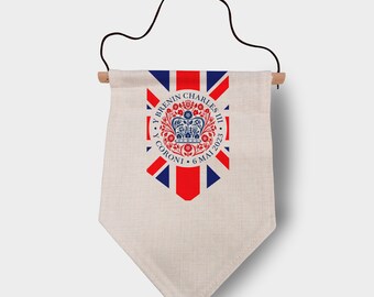 May include: A white fabric pennant with a red, white, and blue Union Jack design. The center of the pennant features a blue circle with a crown, the text "Y Brenin Charles III", and the text "Y Coroni 6 Mai 2023".