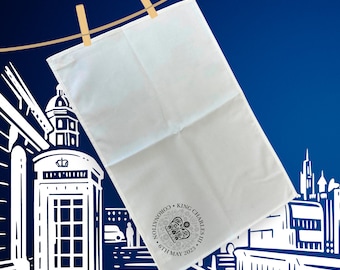 May include: A white tea towel with a black and white image of the coronation of King Charles III. The text on the towel reads "Coronation King Charles III 6th May 2023".